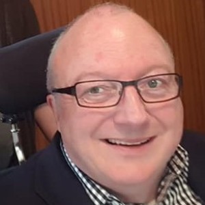 Chris is smiling at the camera, has a bald head, and wears glasses.