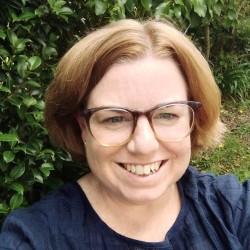 Head and shoulders of woman with strawberry blonde hair in a bob, smiling and wearing glasses.